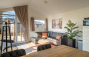 Lyst og moderne opholdsstue i Velthorst Lodge ved Zilverstrand, Belgien, med sofa, spisebord og planter.
