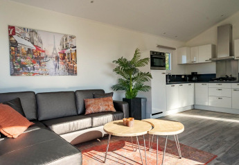 Moderne Velthorst lodge woonkamer aan Zilverstrand, België, met bank, kunst, plant en lichte keuken.
