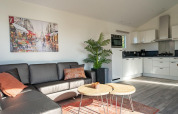 Modern Velthorst lodge living room at Zilverstrand, Belgium, with sofa, art, plant and bright kitchen.