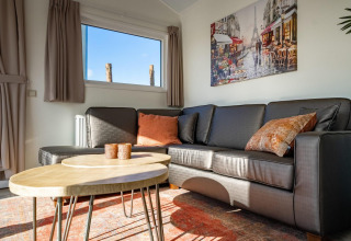 Soggiorno con divano scuro, tavolini rotondi e quadro nella lodge Velthorst a Zilverstrand, Belgio.