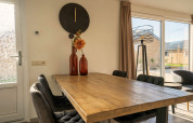 Comedor en la cabaña Velthorst de Zilverstrand, Bélgica, con mesa de madera y grandes ventanales.