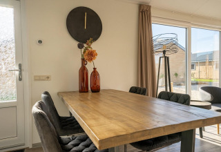 Eethoek in de Velthorst-lodge aan Zilverstrand, België, met houten tafel en grote ramen.