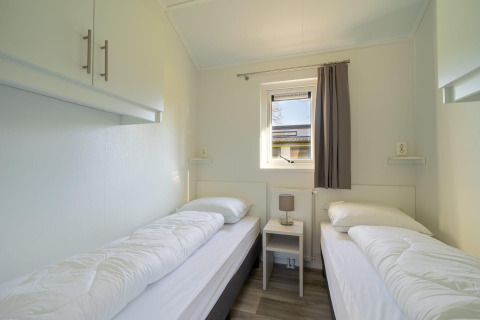 Helles Zimmer mit zwei Einzelbetten, Nachttisch und Fenster in der Velthorst-Lodge am Zilverstrand, Belgien.