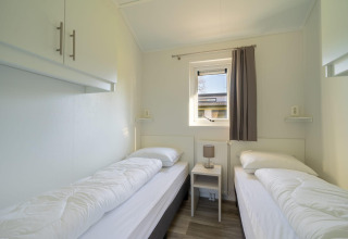 Helles Zimmer mit zwei Einzelbetten, Nachttisch und Fenster in der Velthorst-Lodge am Zilverstrand, Belgien.