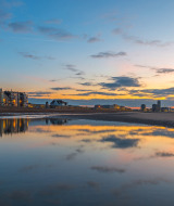 Atardecer en la playa cerca de Oostende, Bélgica, con agua reflejante y edificios iluminados al fondo.