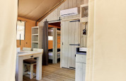 Interieur van een glamping tent met stapelbedden, eettafel, open kast en airconditioning aan de muur.