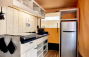 Moderne glampingkeuken met houten wanden, kookplaat, open rekken en een inox koelkast.