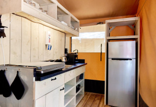 Cucina da glamping moderna con pannelli in legno, fornello, mensole aperte e frigorifero.