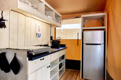 Cocina de glamping moderna con paneles de madera, estufa eléctrica, estantes abiertos y nevera.