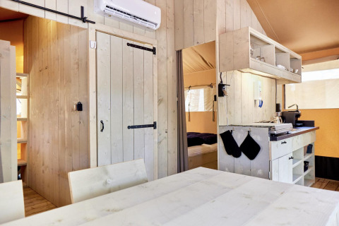 Vista interior de un alojamiento glamping con paneles de madera clara, cocina y dormitorio acogedor.