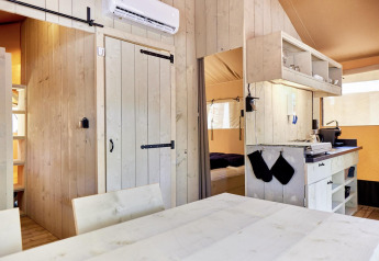 Interieur van een glamping accommodatie met lichte houten wanden, keukenhoek en knusse slaapkamer.