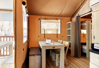 Hébergement glamping lumineux avec meubles en bois, table à manger, lits superposés et vue sur la terrasse.