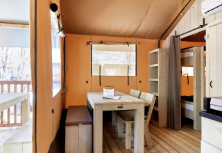 Lichte glampingverblijf met houten meubels, eettafel, stapelbedden en zicht op het terras.