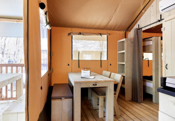 Lichte glampingverblijf met houten meubels, eettafel, stapelbedden en zicht op het terras.
