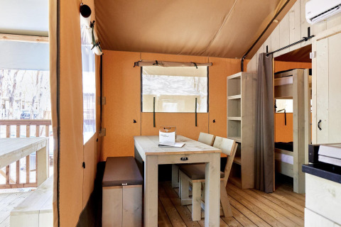 Alojamiento glamping luminoso con muebles de madera, mesa de comedor, literas y vista a la terraza.