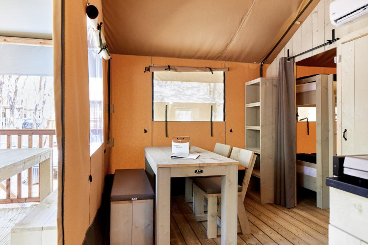 Alojamiento glamping luminoso con muebles de madera, mesa de comedor, literas y vista a la terraza.