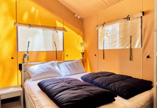 Sistemazione glamping con letto matrimoniale, cuscini bianchi, piumoni neri e luce naturale dalle finestre.
