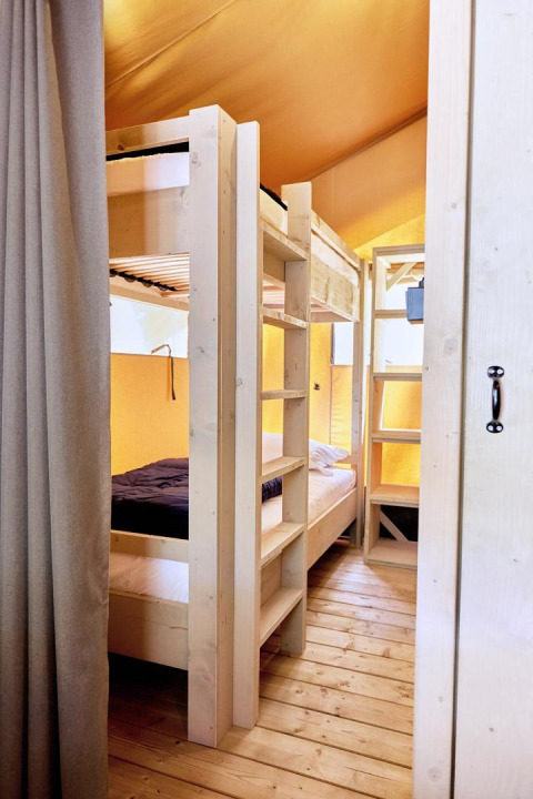 Interior de una tienda de glamping con literas de madera clara, suelo de madera y ambiente acogedor.