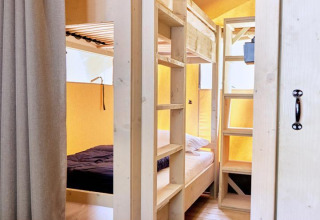 Interior de una tienda de glamping con literas de madera clara, suelo de madera y ambiente acogedor.