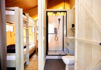 Photo intérieure d’un hébergement glamping avec lits superposés en bois et salle de bain avec douche et WC.