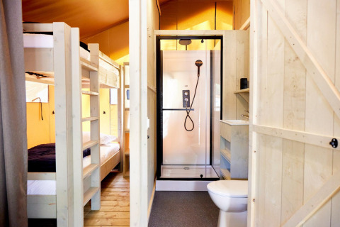 Foto interna di un alloggio glamping con letti a castello in legno e bagno dotato di doccia e WC.