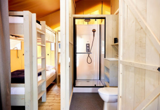 Foto interna di un alloggio glamping con letti a castello in legno e bagno dotato di doccia e WC.
