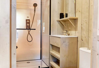 Salle de bain moderne dans un hébergement glamping avec douche, lavabo, miroir et toilettes en bois clair.