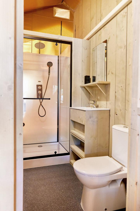 Bagno moderno in una sistemazione glamping con doccia, lavandino, specchio e wc in legno chiaro.