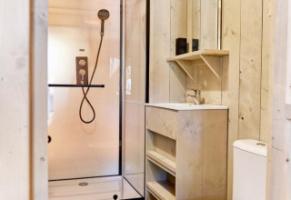 Bagno moderno in una sistemazione glamping con doccia, lavandino, specchio e wc in legno chiaro.