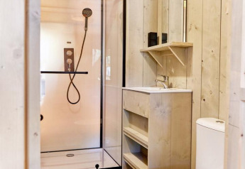 Bagno moderno in una sistemazione glamping con doccia, lavandino, specchio e wc in legno chiaro.