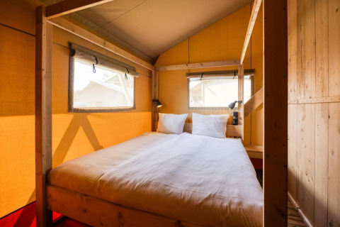 Vista interior del lodge Sunshine en Petite Suisse, Bélgica, con cama cómoda y estructura de madera.