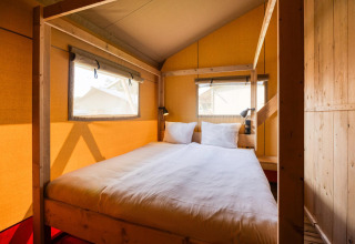 Vista interna della lodge Sunshine a Petite Suisse in Belgio, con letto accogliente e struttura in legno.