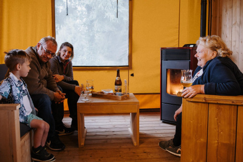 Gezin geniet van drankjes en gezelligheid bij de kachel in lodge Sunshine bij Petite Suisse in België.