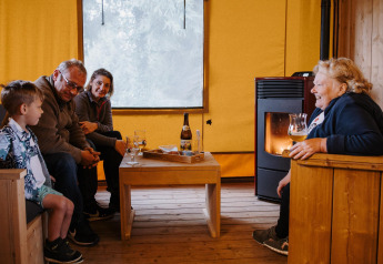 Family enjoying drinks and cozy conversation inside Sunshine lodge at Petite Suisse, Belgium, near the stove.