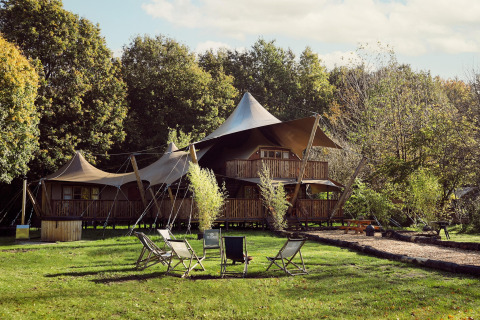 Tente glamping Hacienda au Resort de Parel, Pays-Bas, entourée d’arbres et de chaises de jardin.