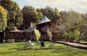 Glamping telt Hacienda ved Resort de Parel i Holland omgivet af træer og udendørs stole på græsset.