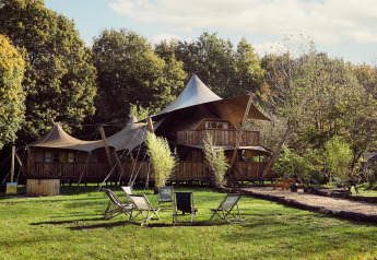 Glamping-Zelt Hacienda im Resort de Parel in den Niederlanden, umgeben von Wald und Gartenmöbeln.