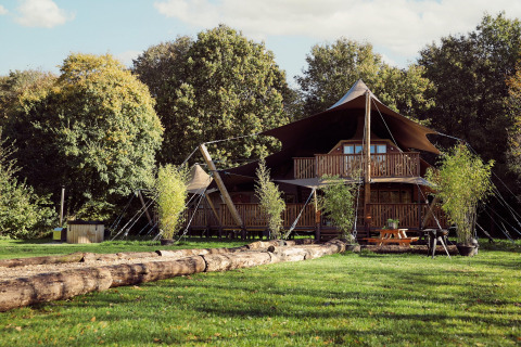 Tienda glamping Hacienda en Resort de Parel, Países Bajos, rodeada de césped y árboles altos.
