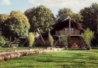 Glamping-Zelt Hacienda im Resort de Parel, Niederlande, umgeben von grüner Wiese und Bäumen.