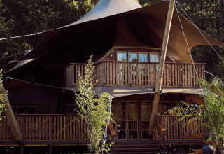 Tente de glamping safari de luxe avec balcon au Resort de Parel aux Pays-Bas, entourée de verdure.