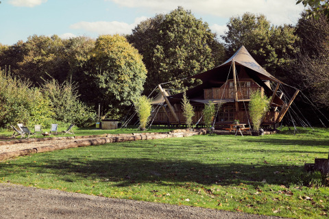 Glamping telt Hacienda ved Resort de Parel, Nederland, omgivet af grønne træer og udendørs siddepladser.