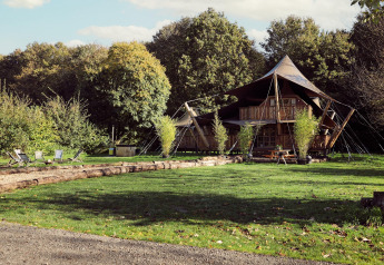 Glamping telt Hacienda ved Resort de Parel, Nederland, omgivet af grønne træer og udendørs siddepladser.