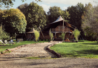 Glamping-Zelt Hacienda im Resort de Parel, Niederlande, umgeben von Rasen, Bäumen und Sitzgelegenheiten.
