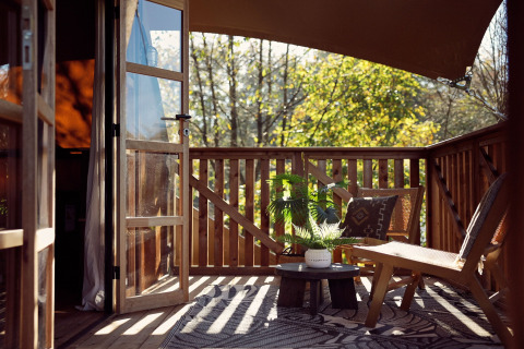 Terraza soleada con sillas de madera, plantas y puertas abiertas en una tienda glamping en Resort de Parel, Países Bajos.