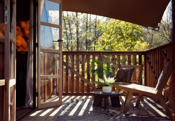 Sonnige Terrasse mit Holzmöbeln, Pflanzen und offenen Türen in einem Glamping-Zelt im Resort de Parel, Niederlande.