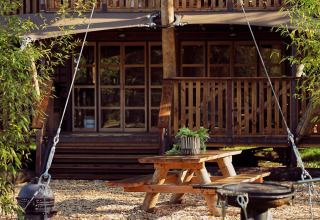 Udendørs spiseområde ved en luksuriøs glamping-telt Hacienda på Resort de Parel, Holland, omringet af træer.