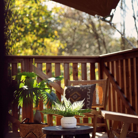 Terraza soleada de madera, plantas verdes, silla de mimbre y mesa en Glamping tent Hacienda, Resort de Parel.