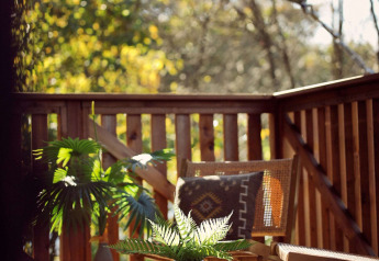 Sonnige Terrasse mit Holzzaun, Grünpflanzen, Korbstuhl und Tisch im Glamping tent Hacienda, Resort de Parel.