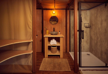 Salle de bain dans une tente safari glamping avec accents boisés, douche moderne et ambiance naturelle chic.