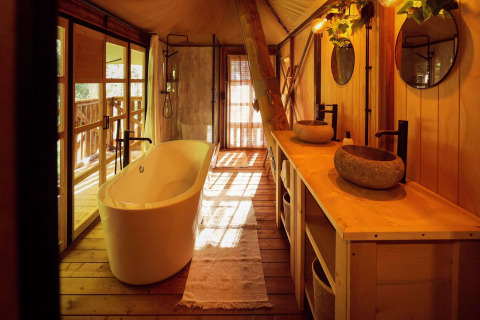 Salle de bain luxueuse dans une tente safari glamping avec baignoire et vasques en pierre au Resort de Parel.